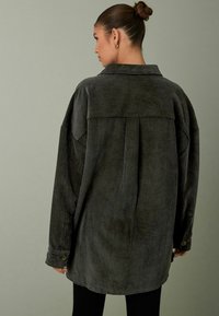 Overmaatse donkergroene corduroy shirtjack met ribbeltextuur, een rugplooi en knoopmanchetten. Getailleerde pasvorm met een klassieke kraag.