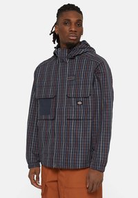 Giubbotto a quadri blu navy con cappuccio, dotato di due tasche frontali, chiusure a bottone e dettagli arancioni. Tessuto leggero con una vestibilità comoda.