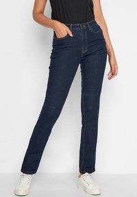 Ciemnoniebieskie dżinsy charakteryzują się klasycznym prostym krojem, stylem pięciu kieszeni oraz kontrastowym żółtym przeszyciem. W połączeniu z białymi trampkami.