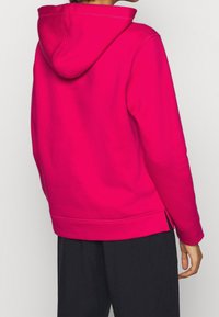Bluza z kapturem z polaru w jasnoróżowym kolorze, z kapturem, o luźnym kroju, długich rękawach i bocznych rozcięciach na dole dla swobody ruchów.