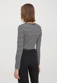 Maglietta a maniche lunghe caratterizzata da righe orizzontali in bianco e nero, scollatura rotonda e design aderente. Abbinata a pantaloni neri a vita alta.