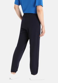 Marina joggingsbyxor i mjukt tyg; elastisk midja och muddar; i kombination med en blå skjorta. Vita sneakers synliga vid vristen.