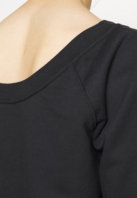 Svart sweatshirt med bred halsringning och korta ärmar, tillverkad av mjukt bomullstyg med en slät textur och minimala sömnadsdetaljer.