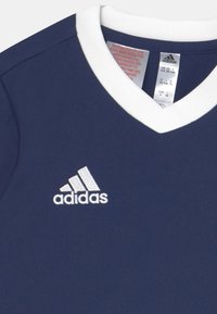Camiseta de color azul marino con un cuello en V blanco, que presenta un logo de Adidas bordado en blanco en el lado izquierdo del pecho. Etiquetas visibles en el interior del cuello.