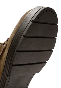 Semelle de chaussure en daim marron avec de larges rainures horizontales et de petits trous circulaires près des orteils et du talon pour l'adhérence.