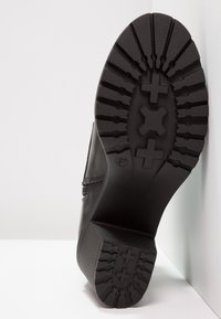 Botín negro con una suela de goma texturizada que presenta un patrón de cruces, parte superior de cuero suave y un ligero tacón. La base muestra un diseño de banda de rodadura pronunciado.