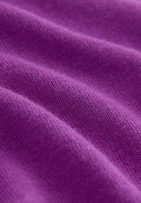 Gros plan sur un tissu violet doux et texturé avec un motif de tricot visible et de légers plis créant des ombres et des reflets.