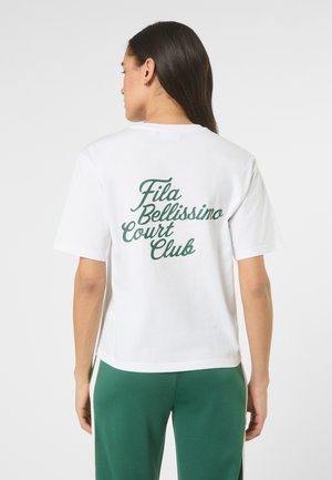 Frau mit langen dunklen Haaren, von hinten gesehen, trägt ein weißes T-Shirt mit der Aufschrift "Fila Bellissimo Court Club" und grüne Hosen mit weißen Streifen.
