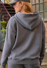 Szara bluza z kapturem, wykonana z miękkiego materiału, o luźnym kroju. Posiada kieszeń kangurzą, ściągacze przy rękawach i na dole.