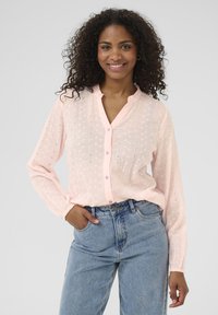 Chemise boutonnière rose pâle avec des motifs tissés, �à manches longues et avec un col. Associée à un jean en denim bleu clair taille haute.