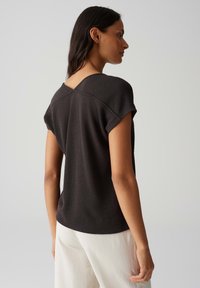 Top nero a maniche corte con tessuto strutturato e scollatura posteriore inclinata, abbinato a pantaloni chiari.