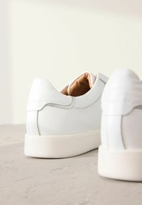Hvide lædersneakers med struktureret overflade, rund hæl og minimalistisk design. Blød tan-farvet inderside og diskret syning.