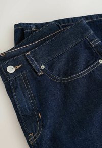 Tmavě modré džíny z denimu s klasickým designem, uspořádáním pěti kapes, měděně zbarveným šitím a decentním kovovým knoflíkem s logem na pásku.
