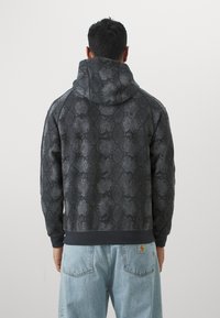Felpa con cappuccio in un motivo a serpente grigio scuro. Caratterizzata da una texture morbida, polsini e orlo a costine. Indossata con jeans di denim azzurro chiaro.