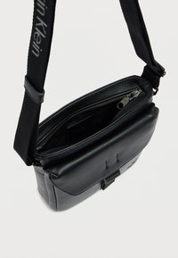 Μαύρη δερμάτινη τσάντα ώμου με υφή, κλείσιμο με φερμουάρ και ρυθμιζόμενο υφασμάτινο λουράκι. Διαθέτει εσωτερικές θήκες για οργάνωση.