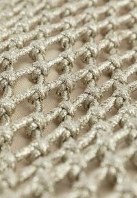 Tissu en maille tissé argent métallique avec un motif en grille, présentant des nœuds serrés et une texture lisse, posé sur un fond neutre doux.