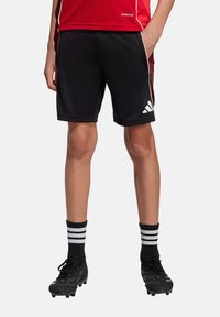 Zwarte sportshorts met rode accentstrepen en wit Adidas-logo, gemaakt van vochtregulerende stof, gecombineerd met zwarte voetbalschoenen en gestreepte sokken.