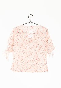Blusa leggera con motivo floreale in rosa tenue, maniche corte e dettagli con fiocco. Collo rotondo e vestibilità fluida.