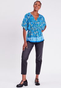 Top peplum floral bleu avec un décolleté en V, des manches courtes et de la broderie, associé à un jean gris foncé ajusté et des chaussures à plateforme noires.