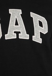 Sweat-shirt noir avec un grand lettrage "GAP" gris. Matière douce au toucher lisse, présentant un détail de couture contrastant autour des lettres.