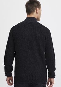 Dunkelgrauer Strickpullover mit hohem Kragen, der ein strukturiertes Muster und gerippte Manschetten aufweist, von hinten vor einem neutralen Hintergrund gezeigt.