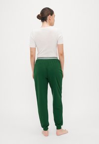Hvit kortermet topp og grønne joggebukser med stripete midje, laget av myk stoff, med avslappet passform og avklipte ankler.