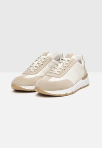 Zapatillas de ante y cuero beige con acentos blancos, punta redonda, diseño con cordones y suela de goma con detalles texturizados y perforaciones.