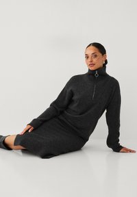 Mørkegrå turtleneck kjole i struktureret stof, med en kvart lynlås foran og lange ærmer med tommelfingerhuller. Glat kant.