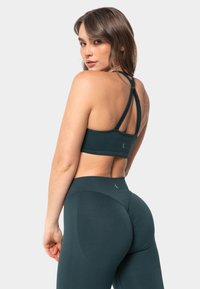 Tirkizni sportski grudnjak s križanim trakama i teksturiranim materijalom; uparen s visokim tajicama koje imaju suptilne uzorke.