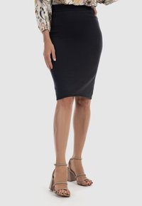 Gonna a tubino nera, di lunghezza al ginocchio, realizzata in tessuto elasticizzato, abbinata a sandali beige con tacco a blocco, indossati a piedi nudi.