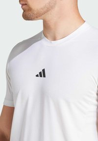 White athletic t-shirt featuring a round neckline, short sleeves, and a black geometric logo on the chest. Smooth fabric texture.