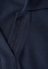 Námořnická polokošile s texturovanou tkaninou. Obsahuje límec a malé vyražené logo na boku, které ukazuje jednoduchý, moderní design.
