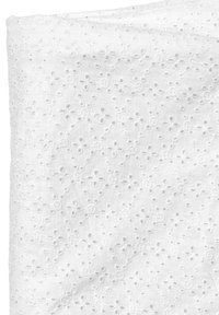 Vit bomullstyg med ett blommigt broderie anglaise-mönster med små hål som skapar en delikat textur genom hela tyget.