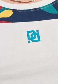 Bela majica s kratkimi rokavi z večbarvnim vzorcem na ovratniku in teal logotipom spredaj. Mehka tkanina, krojen ovratnik.