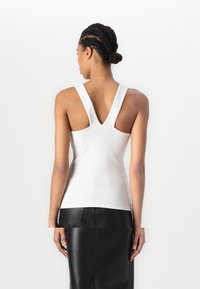 White sleeveless top with wide V-shaped straps, made from a smooth, stretchy fabric, providing a fitted silhouette.