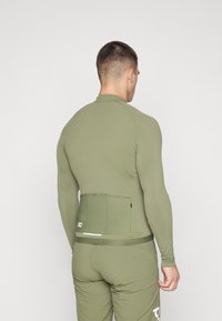 T-shirt de sport à manches longues vert olive au design ajusté, texture lisse et détail de poche à l'arrière. Présente un logo et une bande contrastante au bas.