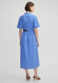 Abito midi a strisce blu e bianche con maniche corte, vita con cintura e colletto. Tessuto morbido e silhouette a forma di A.