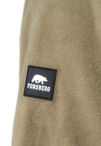 Khaki fleece stof met een gestructureerd oppervlak, voorzien van een zwart rechthoekig patch. Het patch toont een wit berenlogo en de tekst "FORSBERG".
