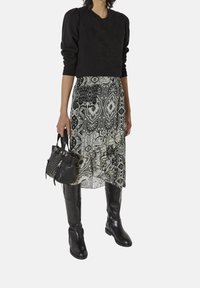 Felpa nera con stampa teschio, sovrapposta a una gonna fluida a fantasia bianco e nero. Stivali neri alla caviglia e una piccola borsa nera completano il look.