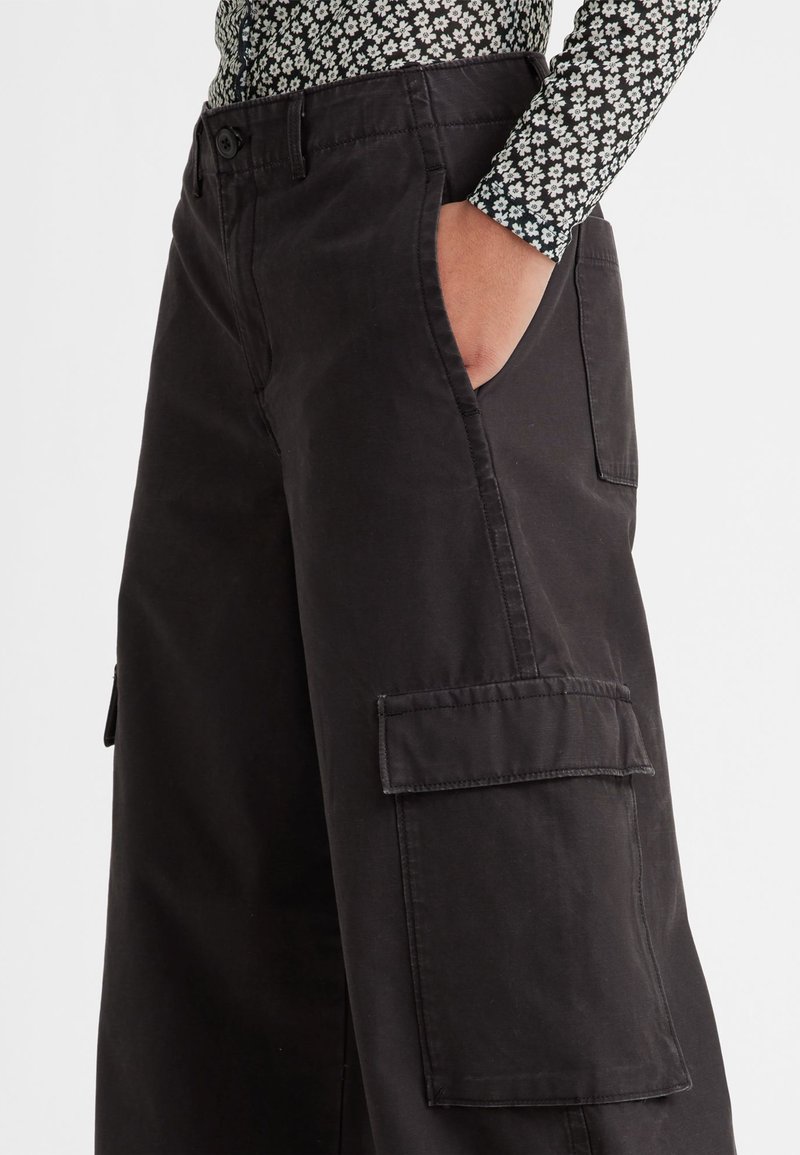 Pantalon cargo noir en tissu coton résistant. Caractéristiques : jambes larges, poches latérales et fermeture à boutons à la taille. Design et texture épurés.
