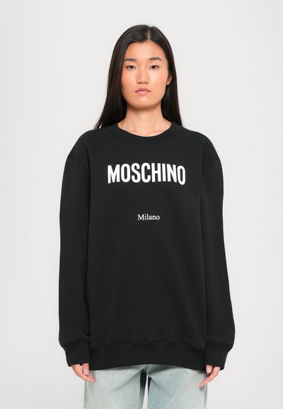 Sweatshirt noir avec le logo "MOSCHINO" blanc et le texte "Milano" en dessous. Doté d'un col ras du cou, de manches longues et de poignets et d'un ourlet côtelés.