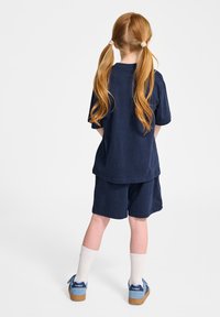 Marinblått bomullströja och shorts-set med avslappnad passform. Kombineras med vita knähöga strumpor och blå sneakers med logodetaljer.