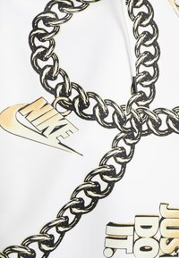 Černý a béžový řetězový vzor na bílém textilu s přesahujícími prvky Nike swoosh a textem "JUST DO IT."