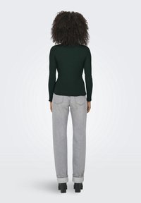 Ciemnozielony prążkowany top z długim rękawem w połączeniu z jasnoszarymi luźnymi dżinsami, z surowym wykończeniem, podwiniętymi mankietami i czarnymi butami na słupku.