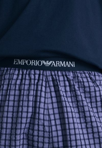 Átmenet nélküli boxeralsó, lila kockás mintázattal, sötétkék rugalmas derékpánttal, amelyen fehér betűkkel az "EMPORIO ARMANI" felirat olvasható, pamut anyagból, laza fazonban.