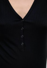 Top in tessuto a coste nero con scollatura a V, caratterizzato da cinque bottoni a pressione in tono argentato lungo il davanti e cuciture testurizzate lungo il collo.
