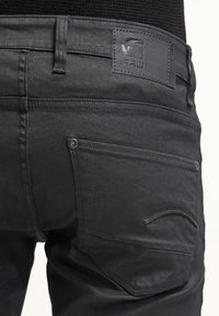 Zwarte denim jeans met een aansluitend ontwerp, voorzien van een leren achterpatch, zakken met gebogen stiksel en een gladde textuur.