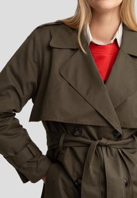 Manteau trench vert olive avec un design croisé, grand col et ceinture nouée à la taille. Comprend des boutons noirs et une texture lisse.