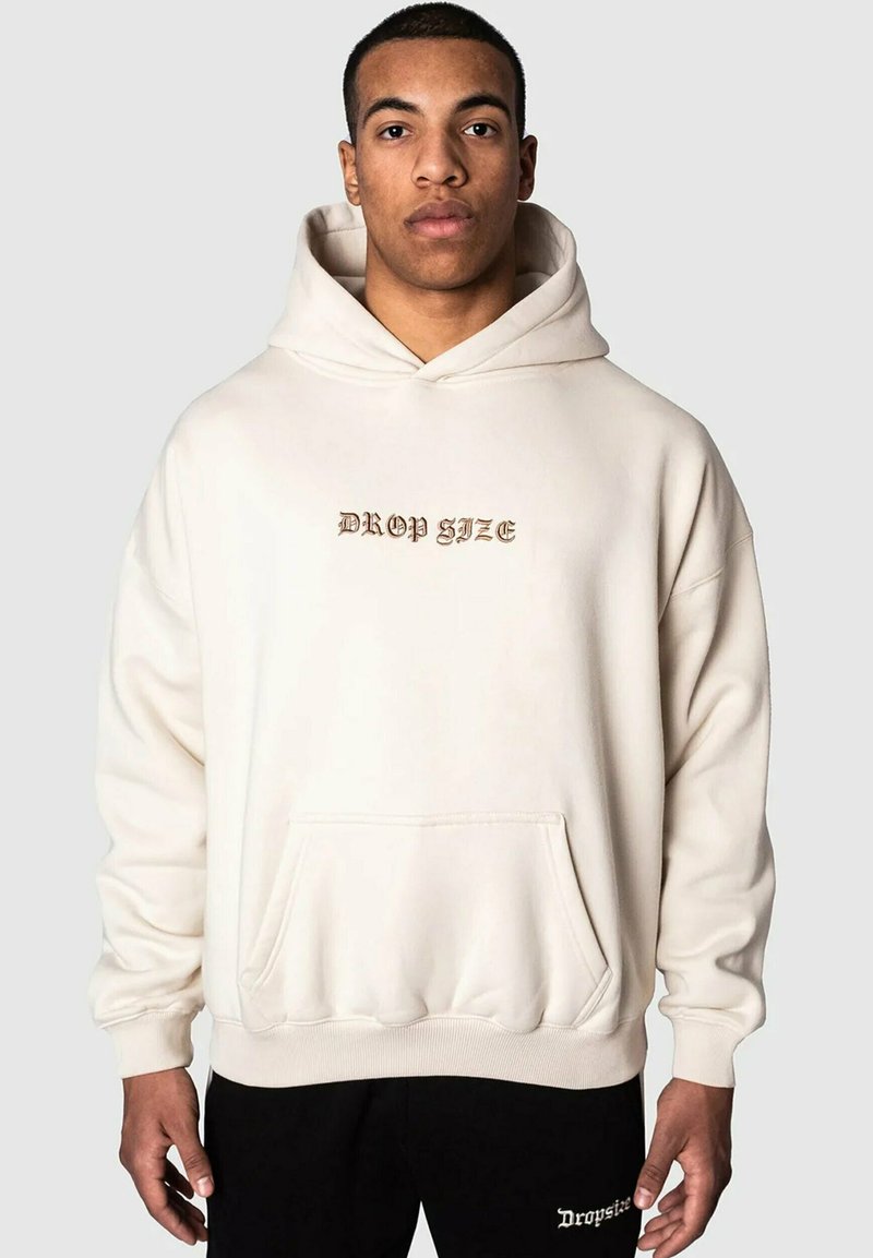 Cremefarbener Hoodie mit einer Vordertasche und dem Text "DROP SIZE" in Gold. Verfügt über eine Kapuze mit Kordelzug sowie gerippte Bündchen und Saum. Weicher Stoff.