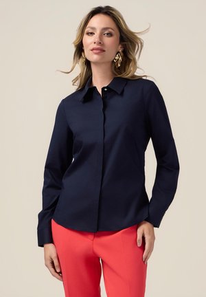 Granatowa koszula z długim rękawem i kołnierzykiem, wykonana z gładkiego materiału; zestawiona z jasnoróżowymi spodniami.